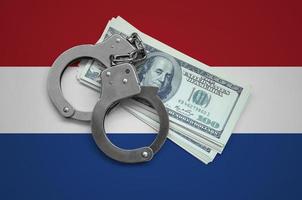 Netherlands flag  with handcuffs and a bundle of dollars. Currency corruption in the country. Financial crimes photo