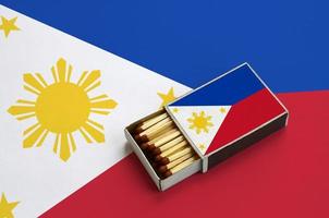 Philippines flag  is shown in an open matchbox, which is filled with matches and lies on a large flag photo