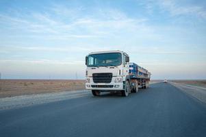 A dump truck with metal barrels on the road against a beautiful sky photo