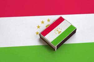 Tajikistan flag  is pictured on a matchbox that lies on a large flag photo