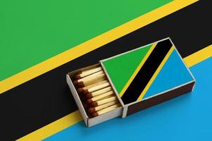 Tanzania flag  is shown in an open matchbox, which is filled with matches and lies on a large flag photo