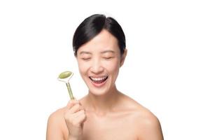 Studio shot of an attractive young asian woman using a jade roller on her face against a white background photo