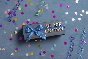 Black Friday text with gift and festive tinsel flat lay on dark cement background photo