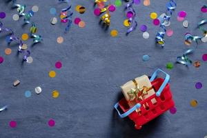 Shopping basket with gift box and festive tinsel flat lay on dark background. Top view photo