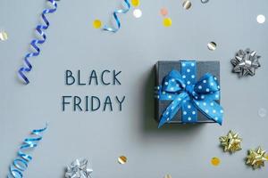 Black Friday text with gift box and festive tinsel flat lay on grey background. Top view photo