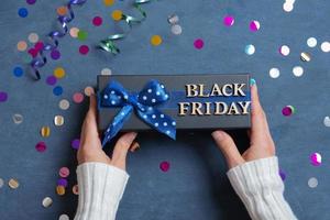 Black Friday text with gift in female hands and festive tinsel flat lay on dark cement background photo