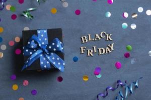 Black Friday text with gift and holiday tinsel flat lay on dark cement background. Top view photo