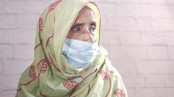 Elderly woman wears a hijab and face mask and looks to the right toward the light video