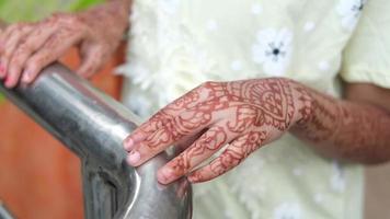 Feminine hands with ornate henna design rest on metal bar video