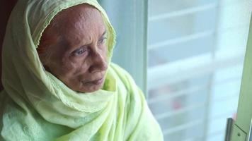 Elderly woman wears a hijab and looks out a window video