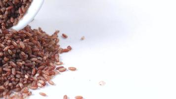 grãos de arroz de jasmim vermelho na tigela e derramado na mesa close-up textura video