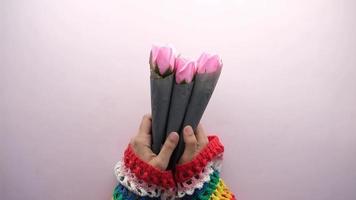 jeune femme aux manches colorées tient des roses roses emballées individuellement dans du papier noir video