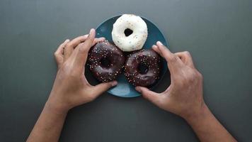 Three iced donuts centered on a table and hands remove two chocolate donuts from the plate video