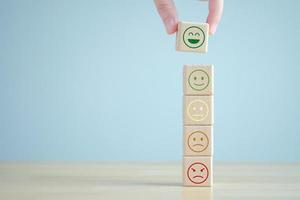 Hand choosing happy face from many emotion on wooden blocks. Positive thinking, Feedback, Satisfaction, Customer service review, Mental health assessment, World mental health day concept. photo