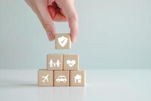 Insurance concept. Protection against a possible eventuality. Hand holding security icon with check mark and House, Car, Family, Healthcare and travel icon on wooden block for assurance life concept. photo