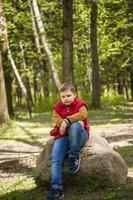 Portrait of a young man in a red tank top in the forest in spring. Walk through the green park in the fresh air. The magical light from the sun's rays falls behind the boy. photo