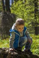 Portrait of a boy in a blue tank top in the woods in spring. Take a walk in the green park in the fresh air. The magical light from the sun's rays falls behind the boy. photo