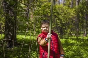 Portrait of a young man in a red tank top in the forest in spring. Walk through the green park in the fresh air. The magical light from the sun's rays falls behind the boy. photo