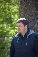 retrato de un hombre en un árbol en el bosque en primavera. dar un paseo por el parque verde al aire libre. la luz mágica de los rayos del sol quedó atrás. espacio para copiar. enfoque selectivo. foto