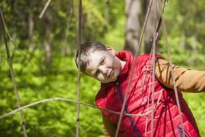 Portrait of a young man in a red tank top in the forest in spring. Walk through the green park in the fresh air. The magical light from the sun's rays falls behind the boy. photo