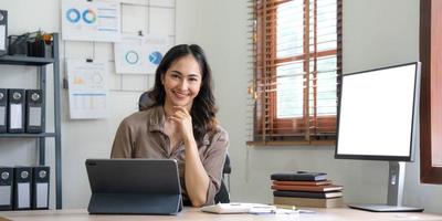 encantadora mujer asiática que trabaja en la oficina usando una laptop mirando la cámara. foto