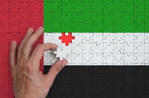 la bandera de los emiratos árabes unidos se representa en un rompecabezas, que la mano del hombre completa para doblar foto