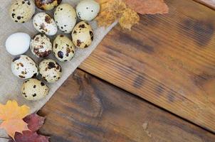 Quail eggs with autumn leaves on sacking on a dark brown wooden surface, top view, empty place for text, recipe photo