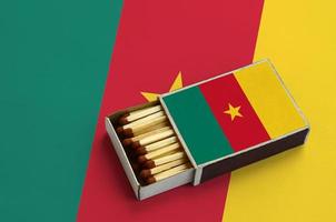 Cameroon flag  is shown in an open matchbox, which is filled with matches and lies on a large flag photo