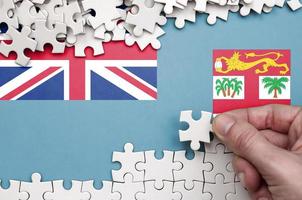 Fiji flag  is depicted on a table on which the human hand folds a puzzle of white color photo