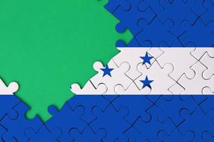 Honduras flag  is depicted on a completed jigsaw puzzle with free green copy space on the left side photo