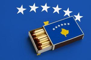 Kosovo flag  is shown in an open matchbox, which is filled with matches and lies on a large flag photo