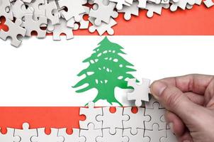 Lebanon flag  is depicted on a table on which the human hand folds a puzzle of white color photo