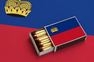 Liechtenstein flag  is shown in an open matchbox, which is filled with matches and lies on a large flag photo