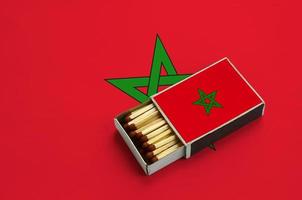 Morocco flag  is shown in an open matchbox, which is filled with matches and lies on a large flag photo