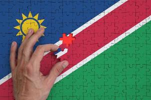 Namibia flag  is depicted on a puzzle, which the man's hand completes to fold photo