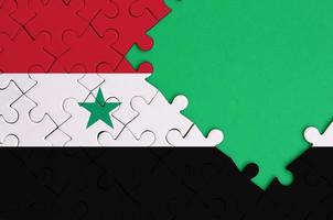 Syria flag  is depicted on a completed jigsaw puzzle with free green copy space on the right side photo