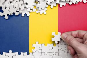 Chad flag  is depicted on a table on which the human hand folds a puzzle of white color photo