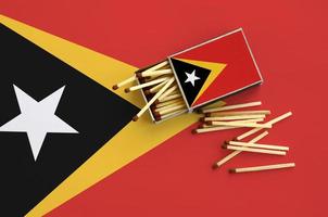 Timor Leste flag  is shown on an open matchbox, from which several matches fall and lies on a large flag photo