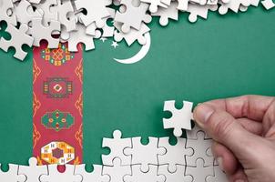 Turkmenistan flag  is depicted on a table on which the human hand folds a puzzle of white color photo