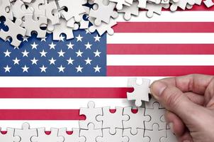 United States of America flag  is depicted on a table on which the human hand folds a puzzle of white color photo