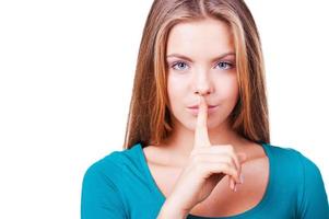 Be quiet Close-up of attractive young woman looking at camera and holding finger on lips while standing isolated on white photo