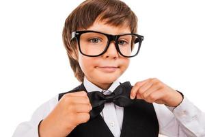 Confident in his skills. Cute little boy adjusting his bow tie and looking at camera while standing isolated on white photo