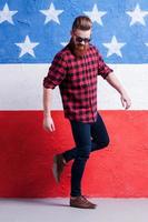 Up fashion. Full length of handsome young bearded man in sunglasses making a step against American flag photo