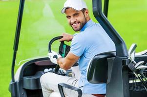 On his way to the next hole. Rear view of young happy male golfer driving a golf cart and looking over shoulder photo