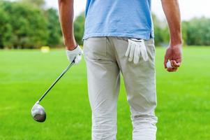 Ready to play. Rear view of male golfer walking away while holding golf ball and driver photo