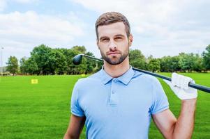 Confident golfer. Confident young male golfer holding driver and looking at camera while standing on green photo