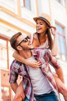 divirtiéndonos juntos. joven feliz cargando a su hermosa novia sobre los hombros y sonriendo mientras camina por la calle foto
