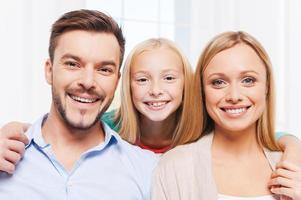 familia feliz. familia feliz de tres que se unen y sonríen mientras están sentados en el interior foto