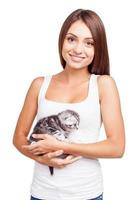 I love my furry little friend. Beautiful young woman holding little kitten in hands and looking at camera with smile while standing isolated on white background photo