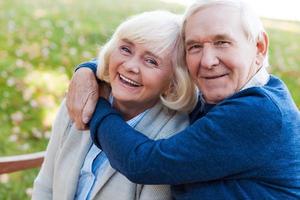 que el amor dure para siempre. feliz pareja de ancianos uniéndose entre sí y sonriendo mientras se sientan juntos en el banco del parque foto